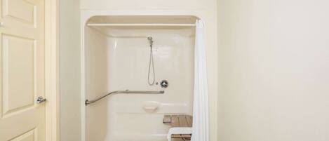 A bathroom with a walk-in shower, a grab bar, a bench, and a door.