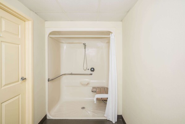 A bathroom with a walk-in shower, a grab bar, a bench, and a door.