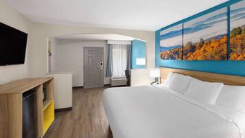 Habitación de hotel con una cama grande, un escritorio con silla, un televisor de pantalla plana y un cuadro de follaje otoñal en la pared.