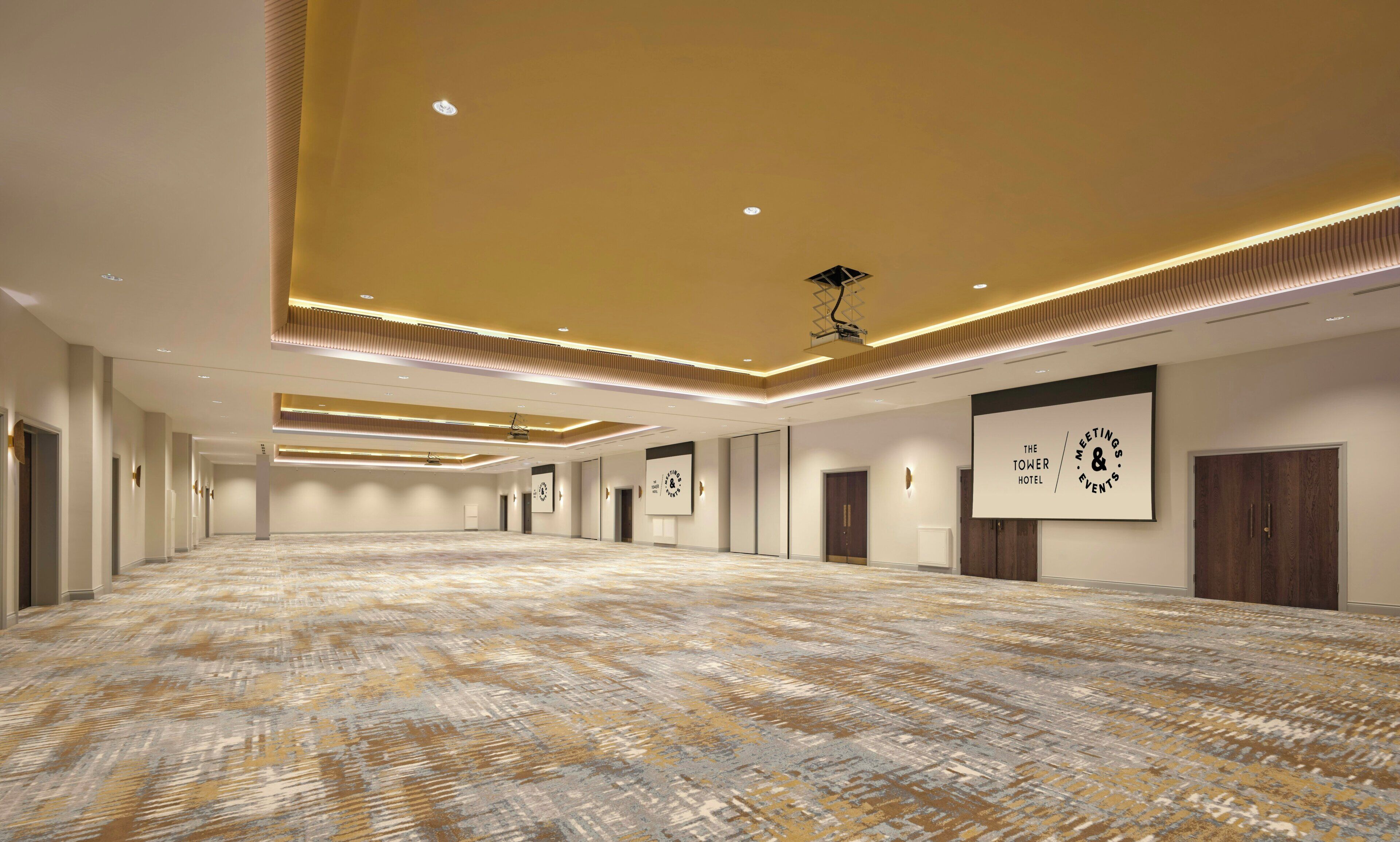 A spacious hotel lobby with a patterned carpet, recessed lighting, and a large clock on the wall.