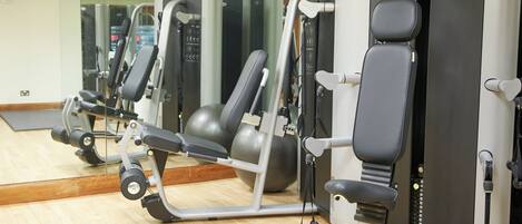 A gym with exercise machines, a mirror, and a wooden floor.