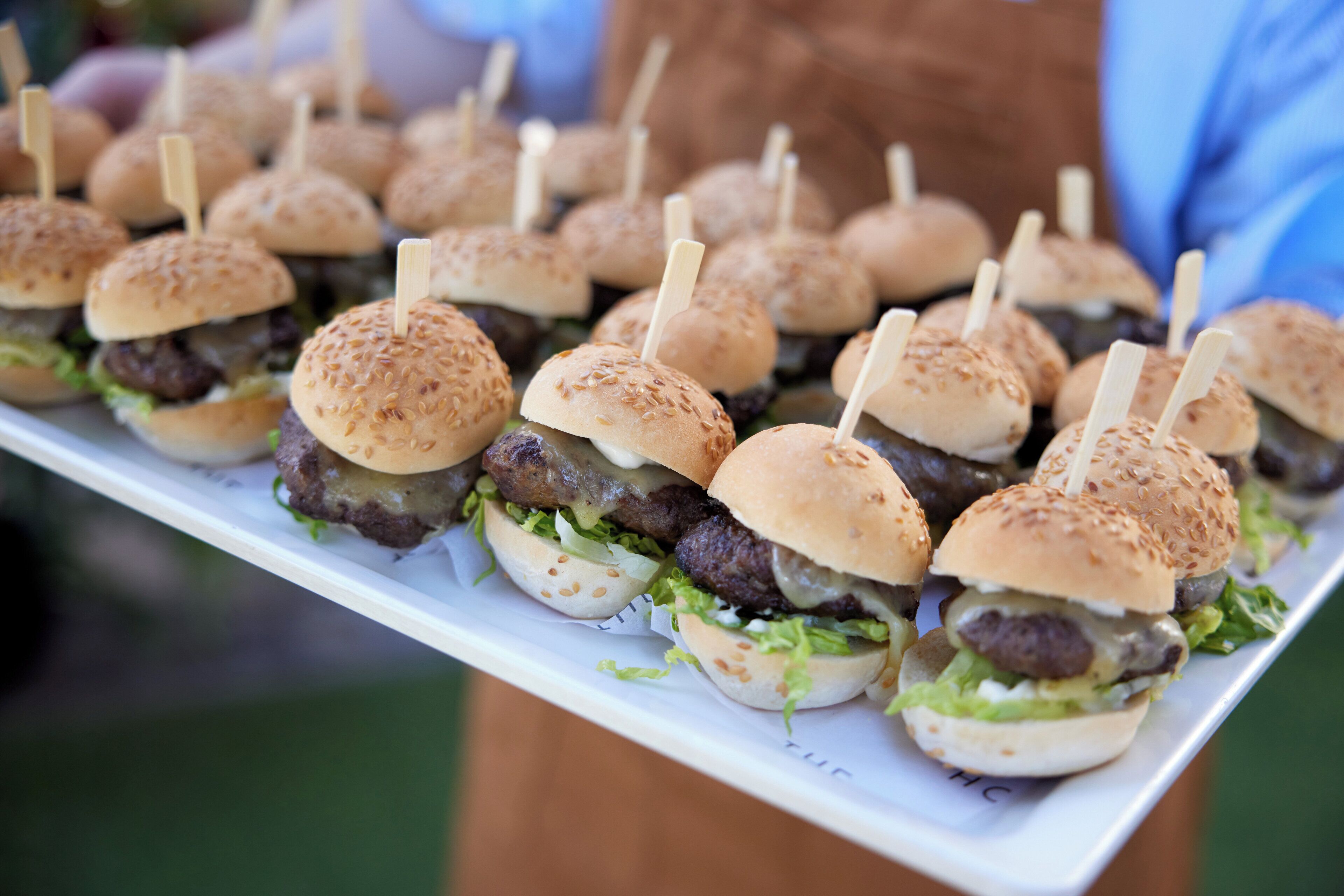 Een schaal met kleine burgers, sesamzaadbroodjes en cocktailprikkers.
