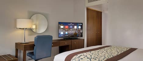 Habitación de hotel con cama, escritorio con silla, televisor mostrando una aplicación del hotel y armario.
