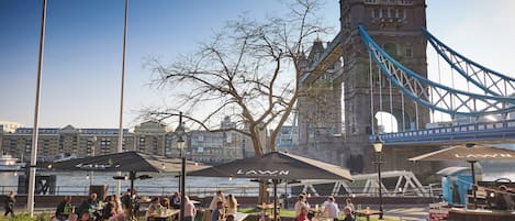 Outdoor seating with umbrellas, a view of a historic tower, and a river.