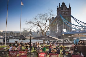 Outdoor seating with umbrellas, a view of a historic tower, and a river.
