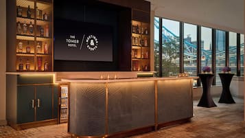 A modern bar area with a large screen displaying 'The Tower Hotel Meetings & Events' branding, surrounded by shelves of liquor bottles.