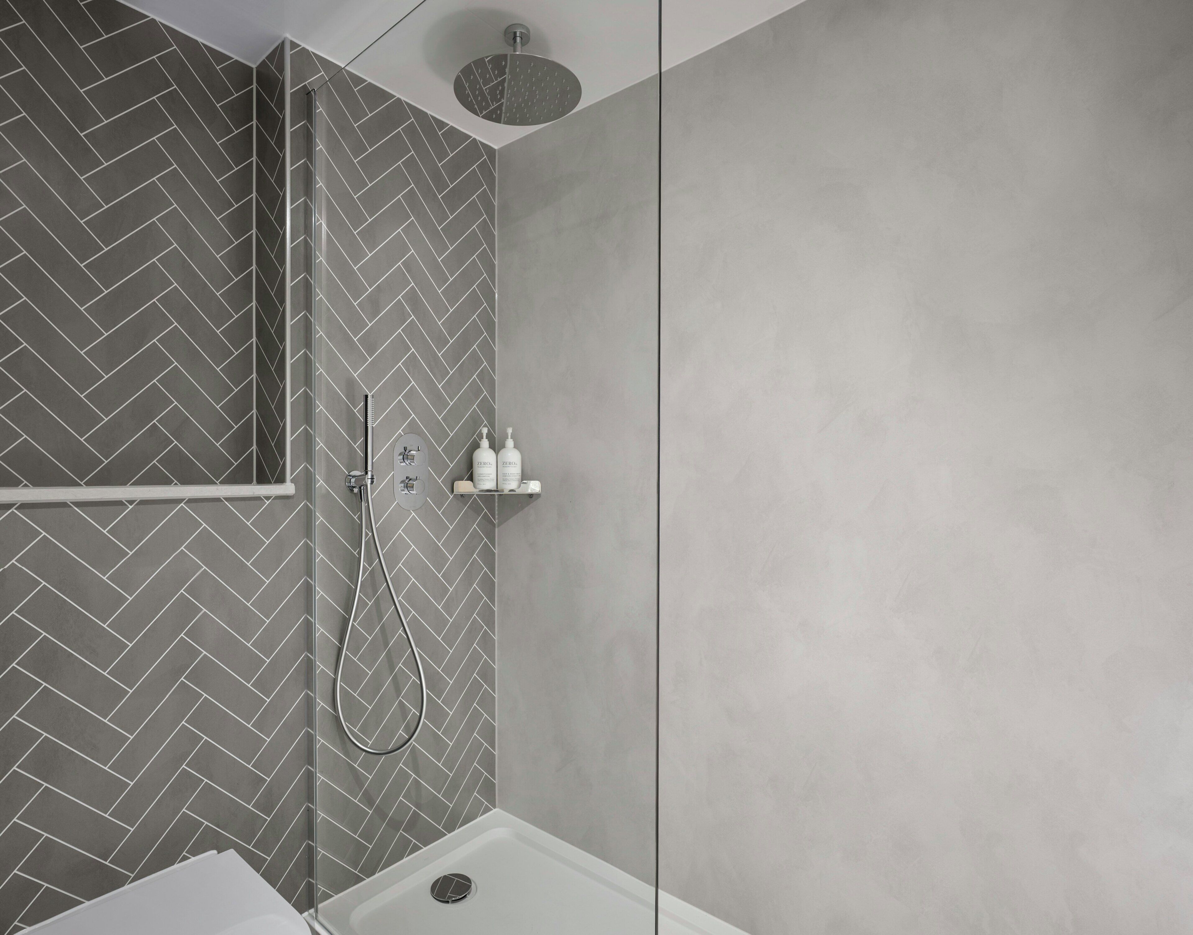 A modern bathroom with a herringbone tile pattern, a shower with a handheld showerhead, and a toilet.
