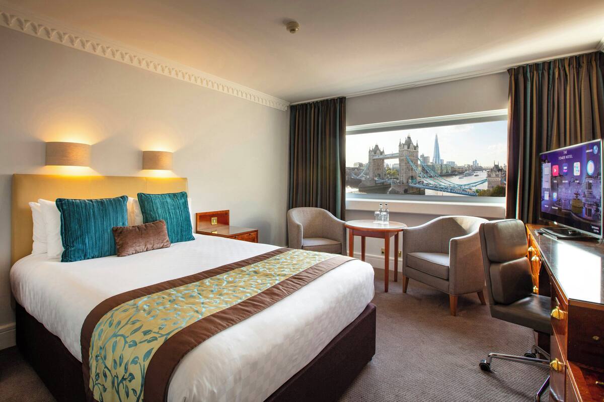 A hotel room with a large bed, a desk with a TV, a chair, and a view of a bridge.