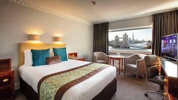 Quarto de hotel com uma cama grande, uma escrivaninha com televisão, uma cadeira e vista para uma ponte.