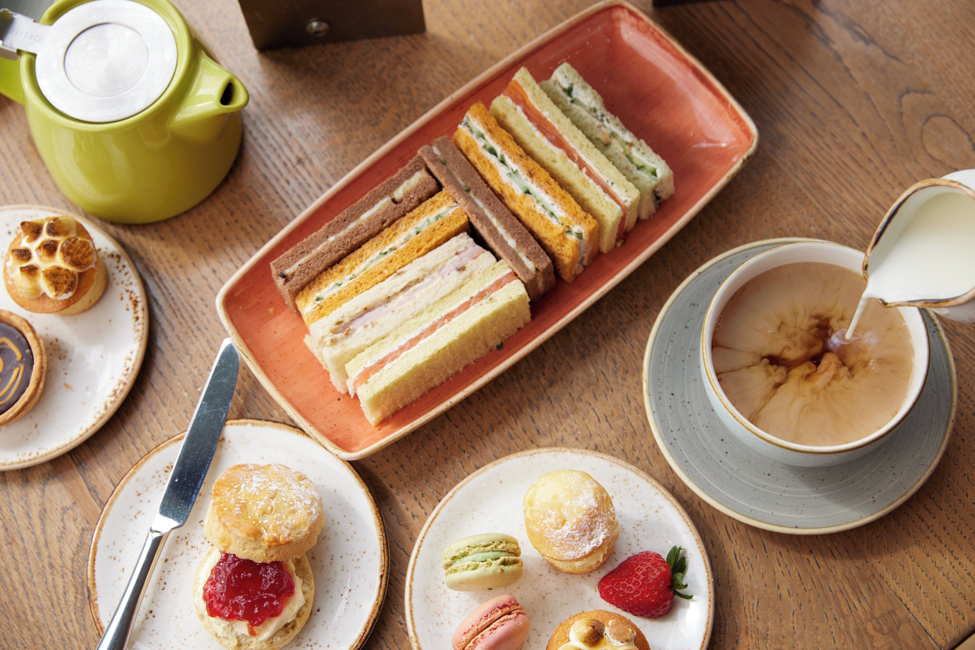 A table with sandwiches, scones, and a teapot.