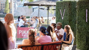 An outdoor seating area with tables and chairs, surrounded by a hedge and a sign with 'PIMM' visible.