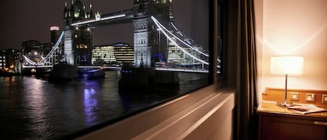 A view of the Tower Bridge at night from inside a room with a lamp on a bedside table.