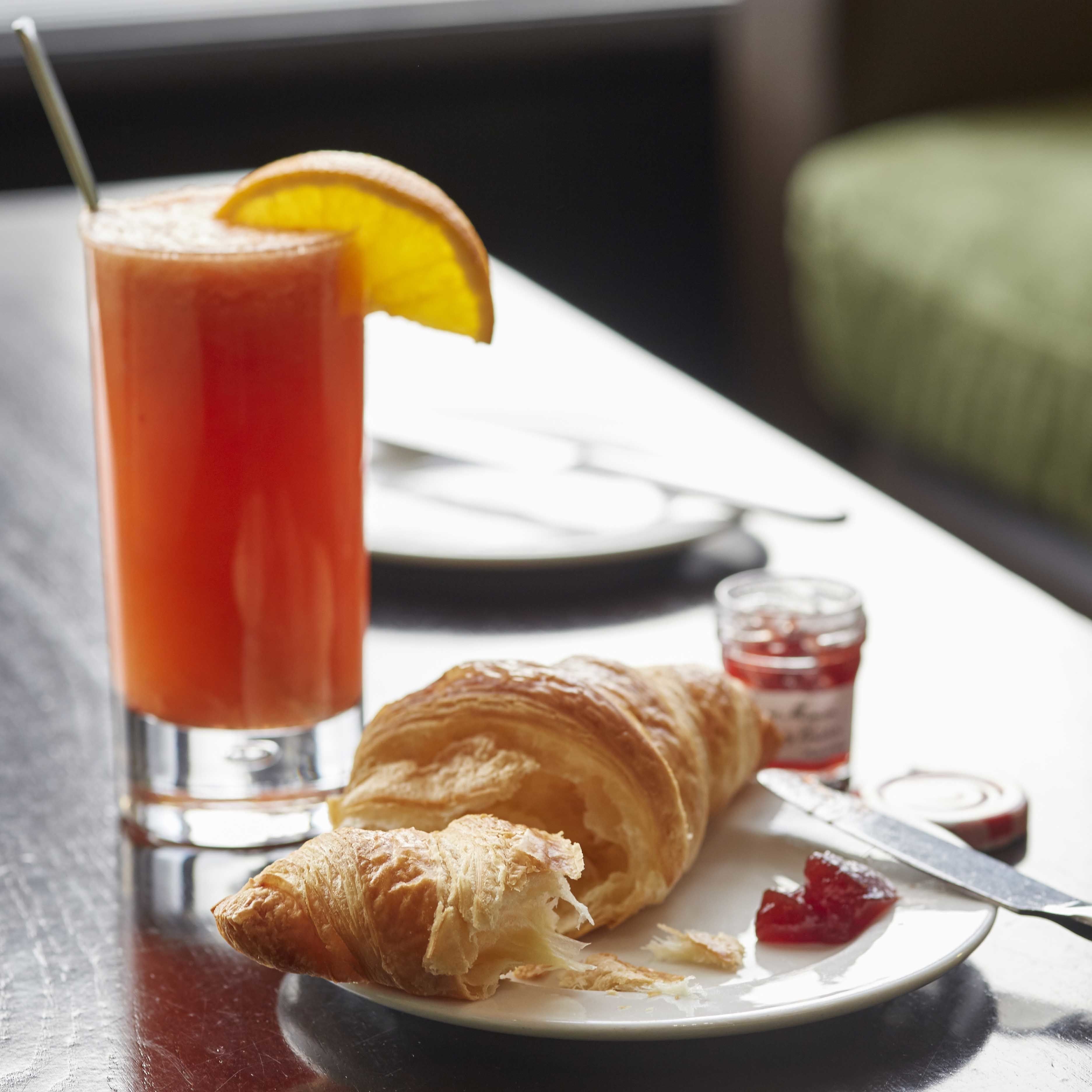 A croissant on a plate with a knife and a glass of orange juice with a lemon slice.