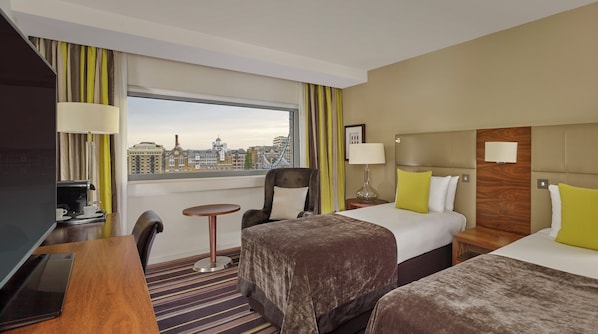 Une chambre d’hôtel avec un lit, un bureau doté d’une machine à café, une chaise, une petite table et une vue sur le paysage urbain.
