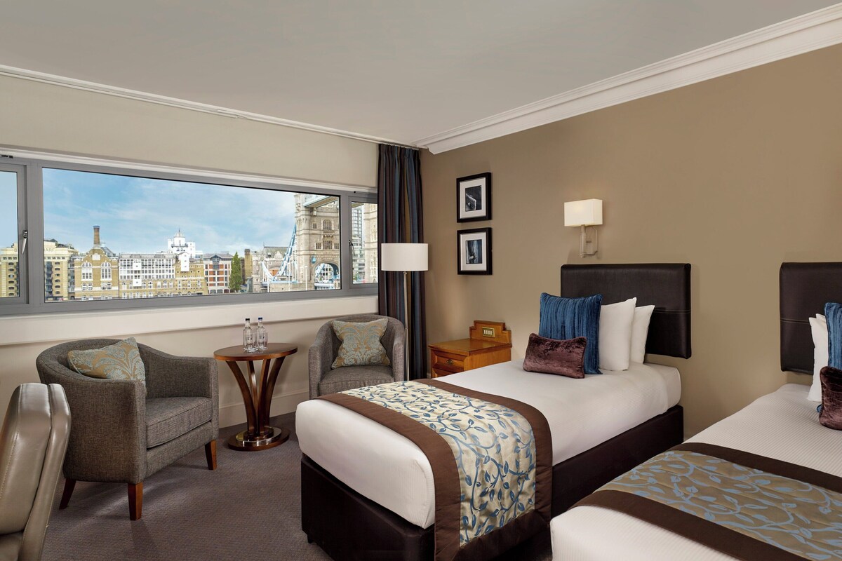 A hotel room with a large window, a bed, a chair, a small table, and a television.
