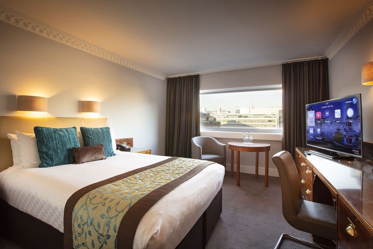 A hotel room with a large bed, a desk with a TV, a chair, and a small table.
