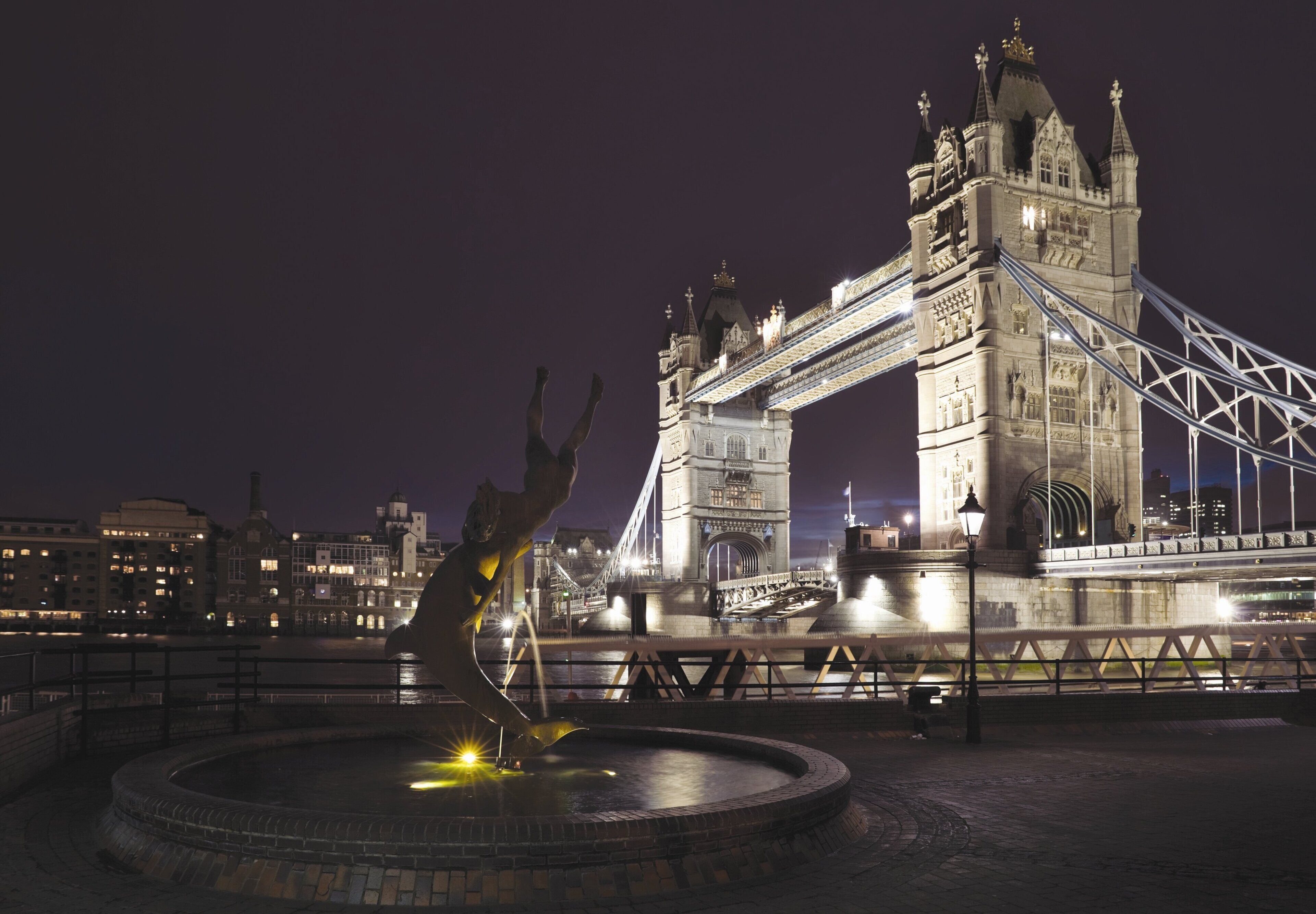 A nighttime view of a historic bridge with a large statue in the foreground.