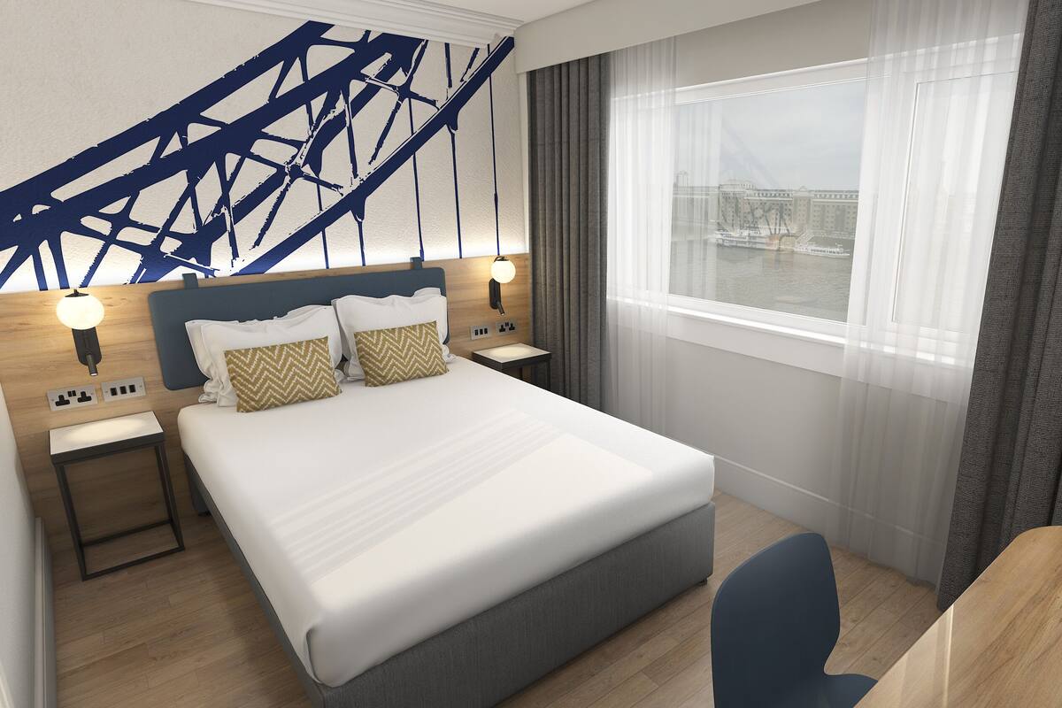 A modern hotel room with a large bed, two bedside tables with lamps, a desk, and a view of a cityscape through the window.