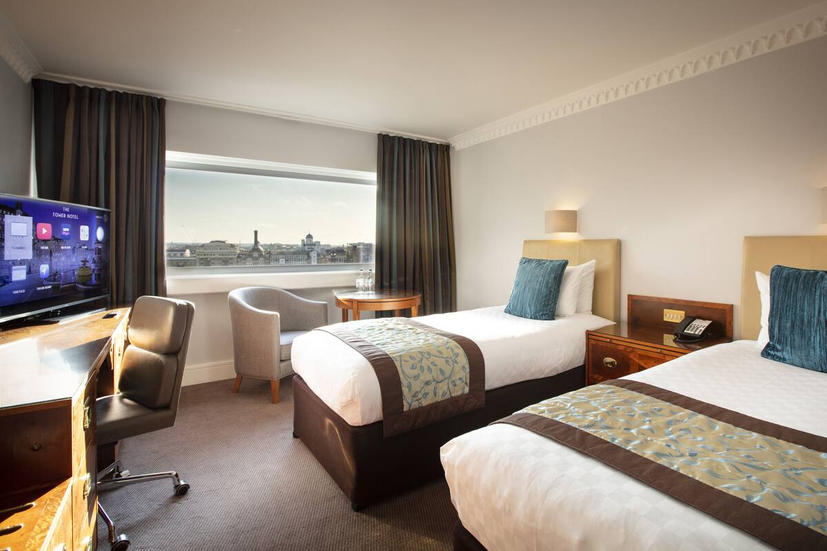 A hotel room with two beds, a desk with a TV, a chair, and a view of the city.