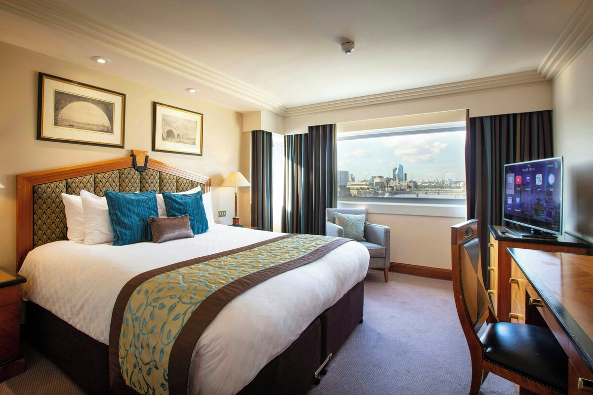 Quarto de hotel com uma cama grande, uma mesa com televisão, uma cadeira e vista para a cidade.