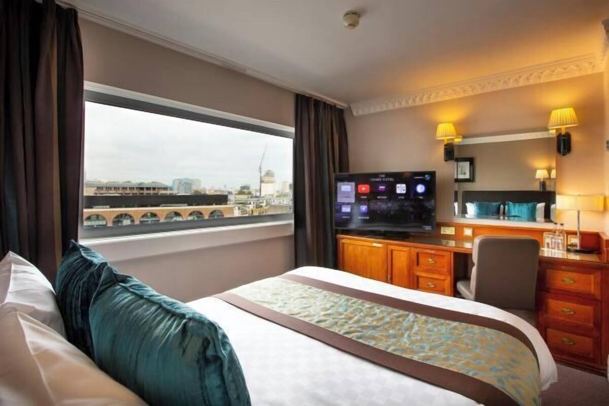 A hotel room with a bed, a desk, a television, and a view of a bridge.