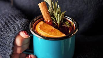 Une personne tenant une tasse bleue contenant une tranche d’orange et un bâton de cannelle.