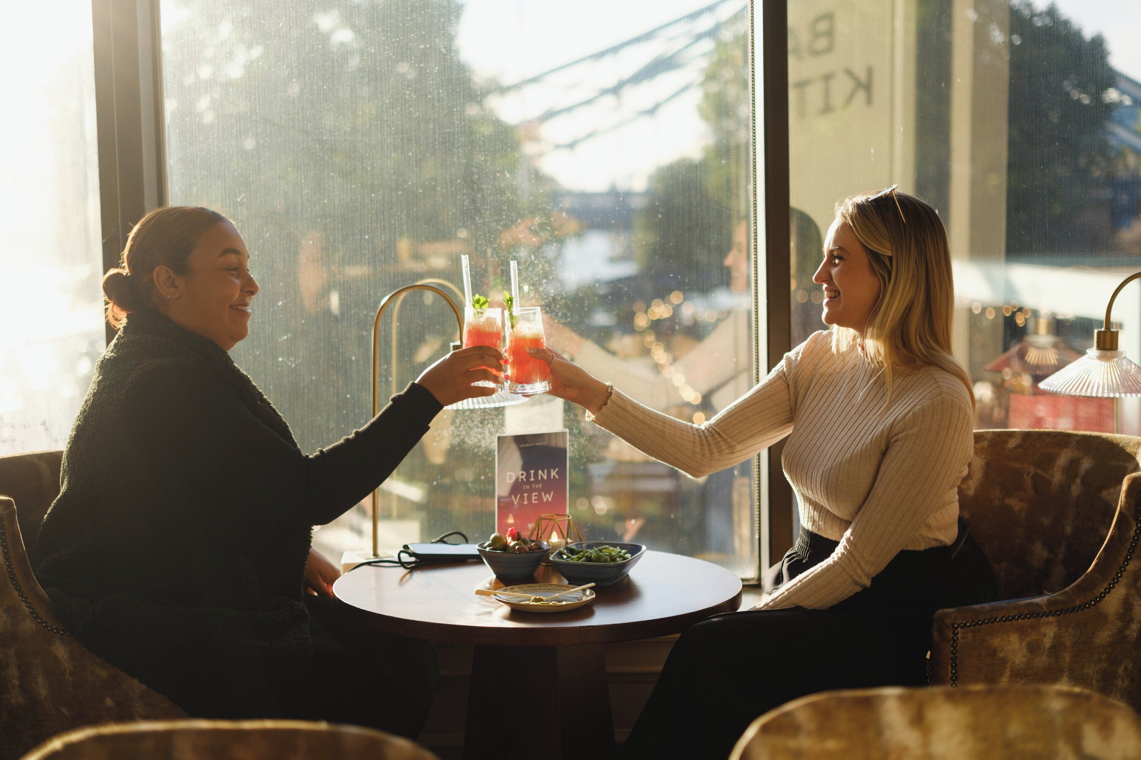 Two people sitting at a table with drinks, a menu, and a bowl of food.