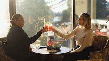 Two people sitting at a table with drinks, a menu, and a bowl of food.
