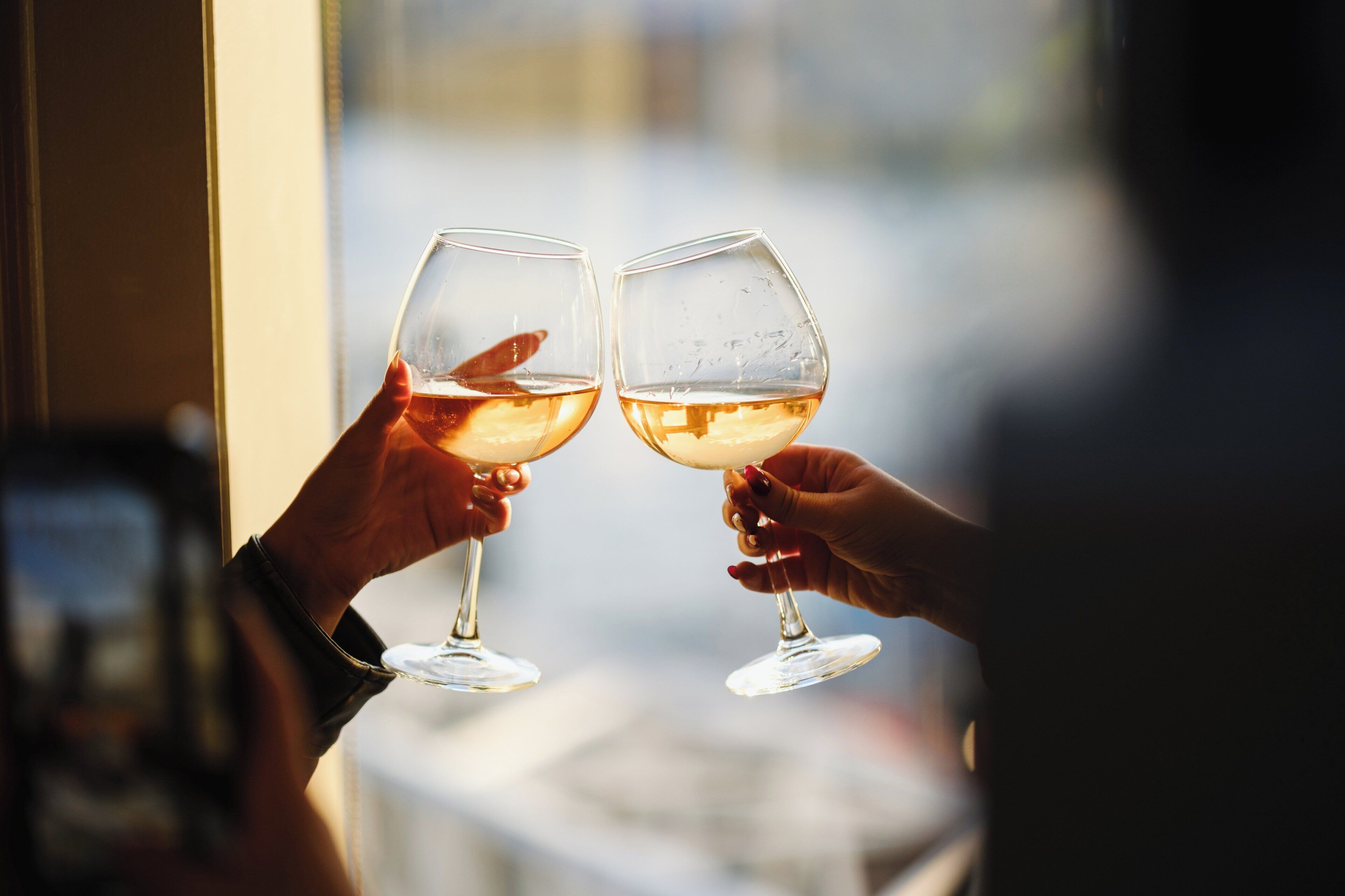 Dos manos sosteniendo copas de vino, una con un objeto rojo en su interior, y un fondo borroso que sugiere un ambiente interior.
