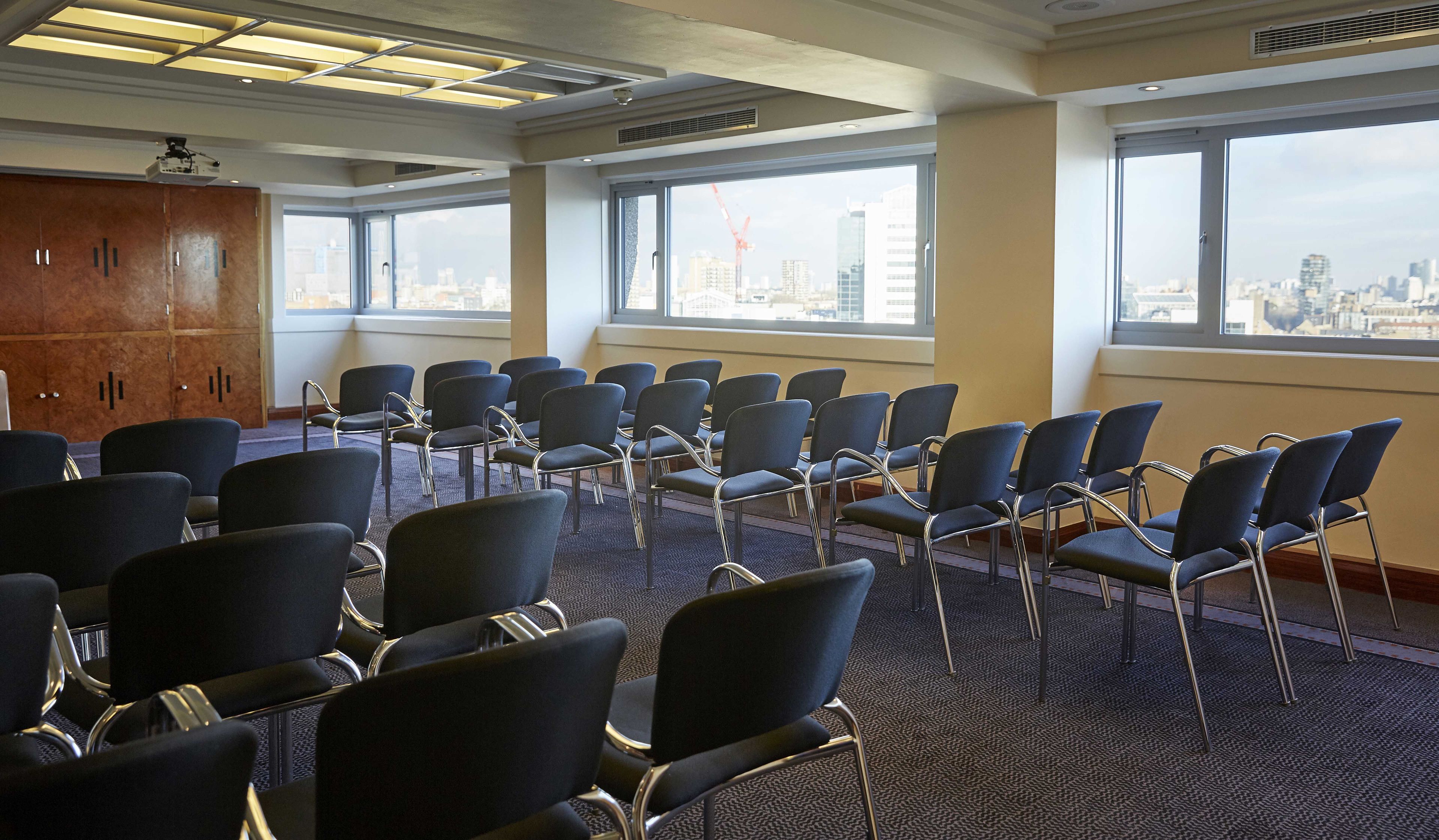Un salón de conferencias con filas de sillas, ventanas amplias con vistas a la ciudad e iluminación empotrada en el techo.