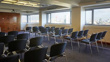 Une salle de conférence avec des rangées de chaises, de grandes fenêtres donnant sur la ville et un plafond doté d’un éclairage encastré.
