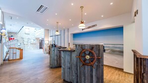 A reception area with wooden reception desks, a ship's wheel decoration, and a blue wall mural. - Dorint Hotel Alzey/Worms (Alzey)