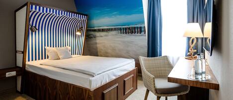 A hotel room with a bed, a desk with a chair, a large window with curtains, and a wall mural of a pier.
