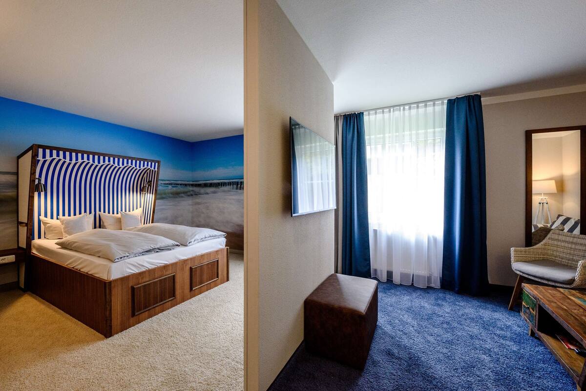 Ein Hotelzimmer mit Bett, einer kleinen Sitzecke, einem Fernseher und Meerblick durch das Fenster.