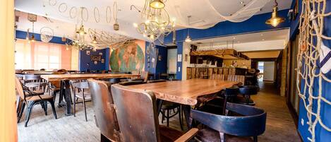A restaurant interior with wooden tables and chairs, hanging light fixtures, and a large world map on the wall.