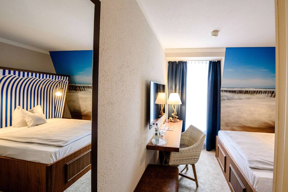 Ein Hotelzimmer mit zwei Betten, einem Schreibtisch mit Lampe, einem Sessel und Meerblick durch das Fenster.