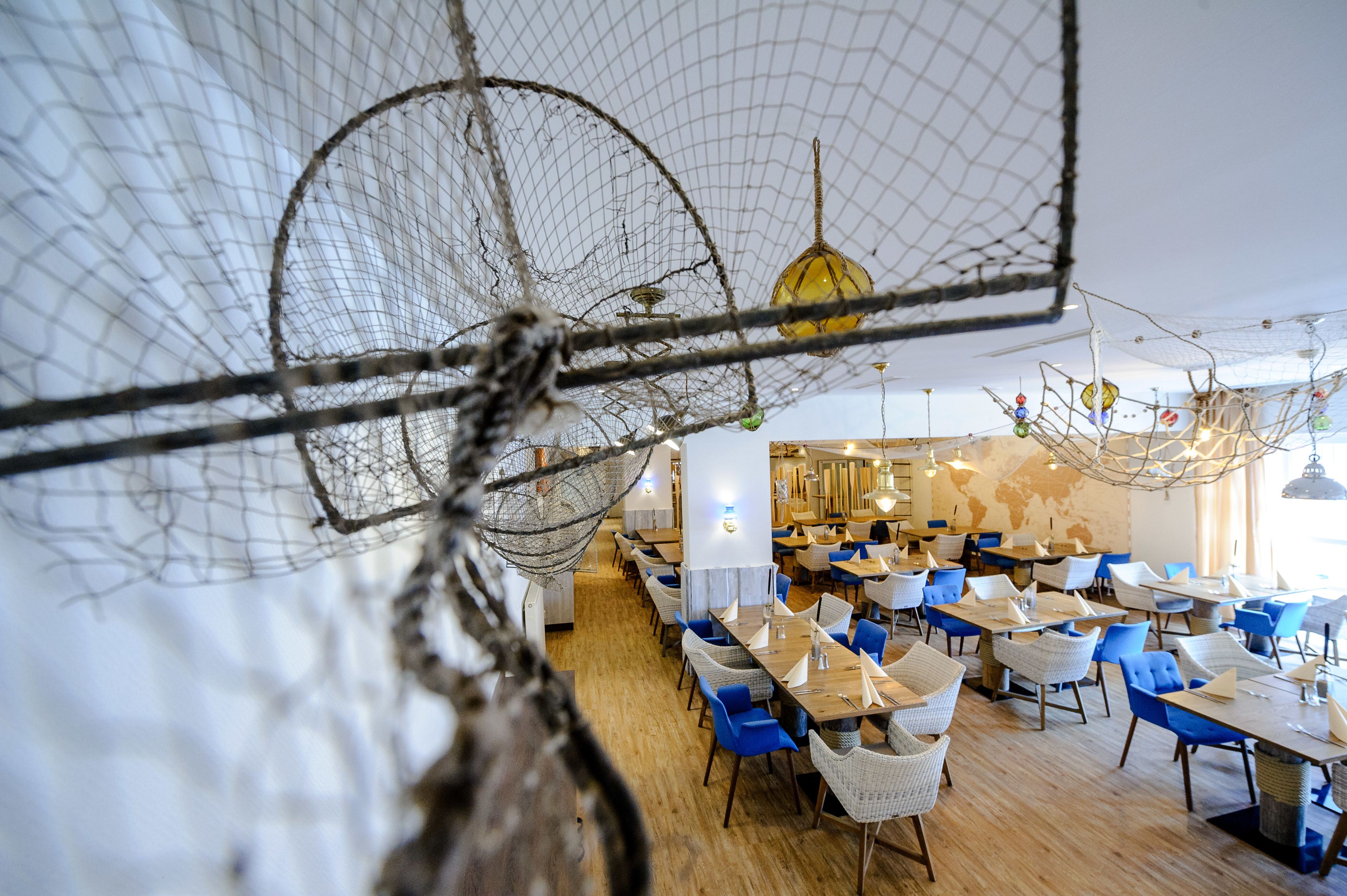 Un restaurante con una decoración moderna, que presenta sillas azules y blancas, mesas de madera y un diseño de techo original con elementos colgantes.