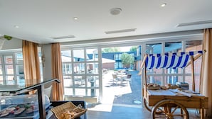 A hotel lobby with a buffet area, large windows, and a view of the outdoor patio. - Dorint Hotel Alzey/Worms (Alzey)