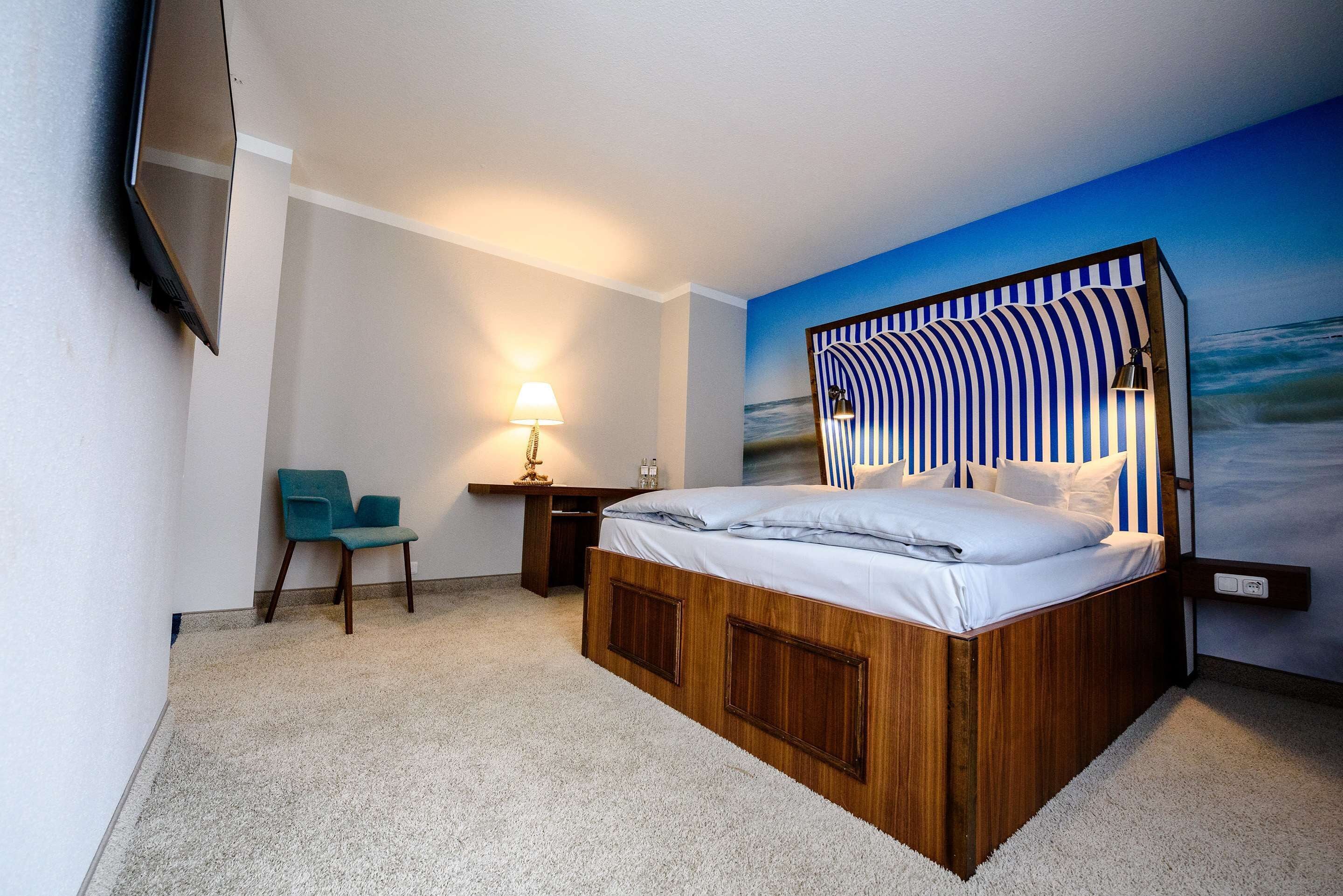 A bedroom with a large bed, a desk, a chair, and a TV mounted on the wall.