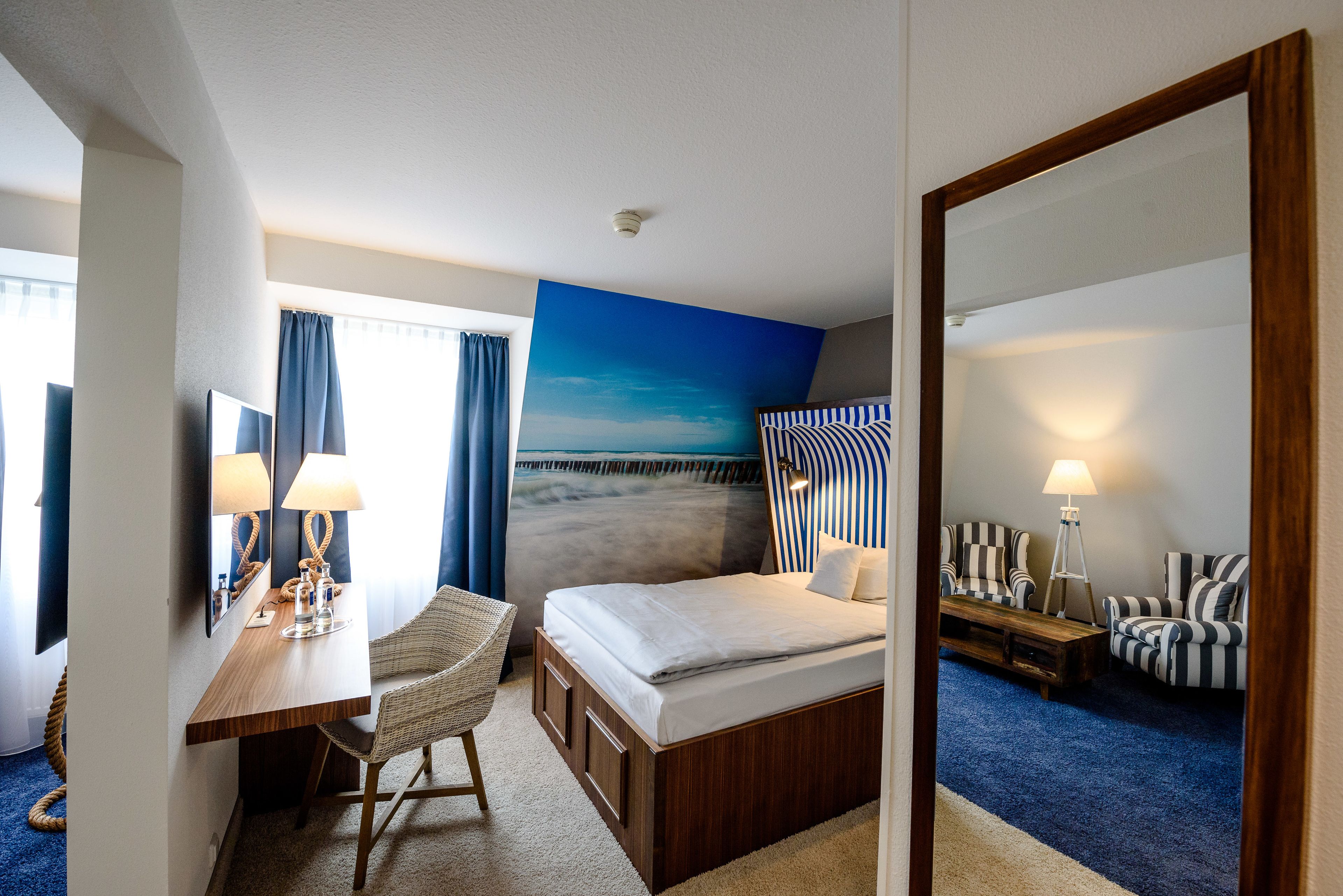 Habitación de hotel con cama, escritorio con lámpara, silla, sofá y un espejo grande.