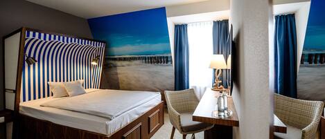 Habitación de hotel con una cama, un escritorio, dos sillas, una lámpara y vista al mar por la ventana.