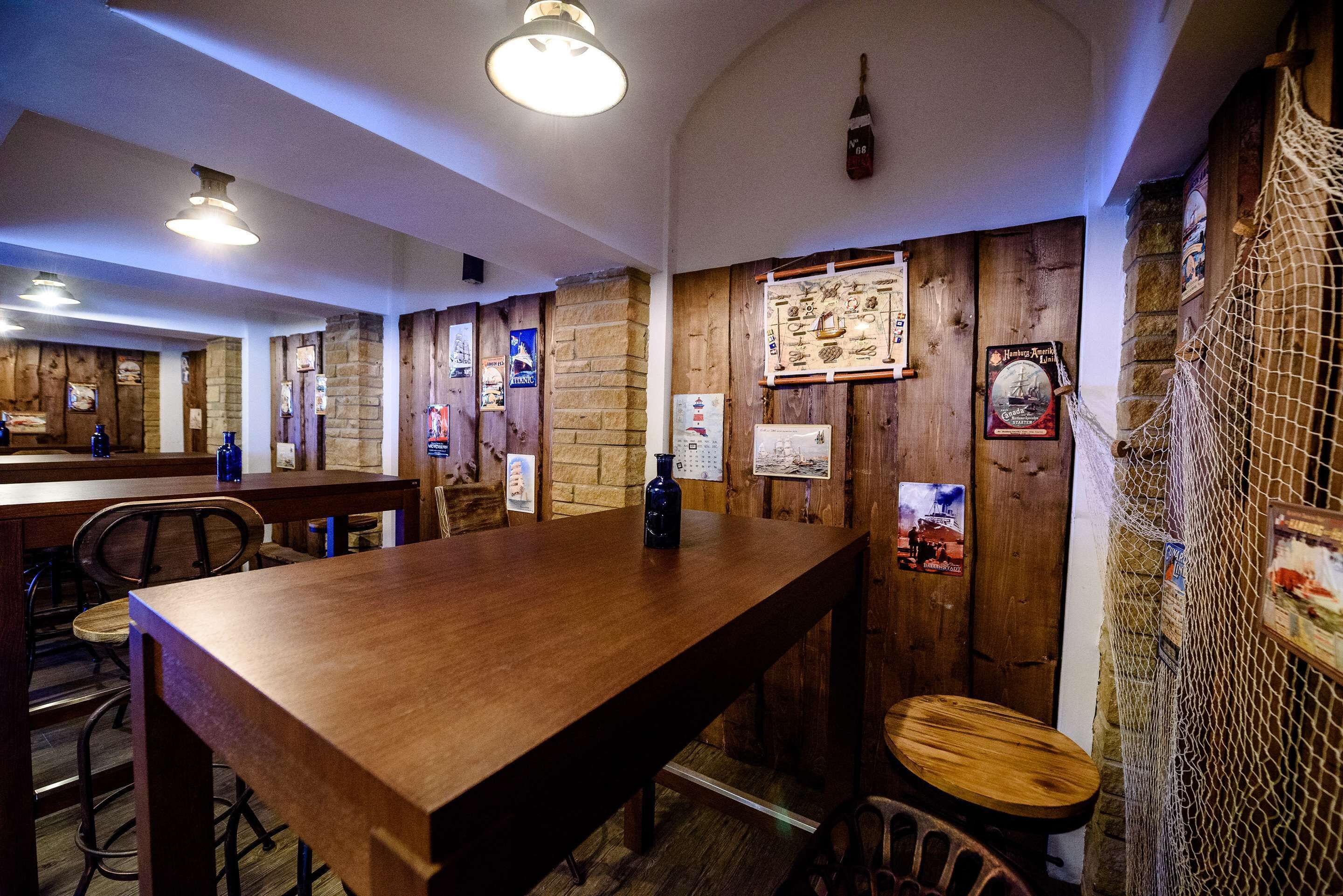 Un interior de madera con una larga mesa y sillas, paredes de piedra, y varios carteles y letreros.
