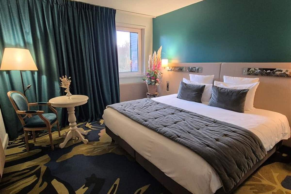 Une chambre d’hôtel avec un grand lit, une chaise, une petite table et une fenêtre.