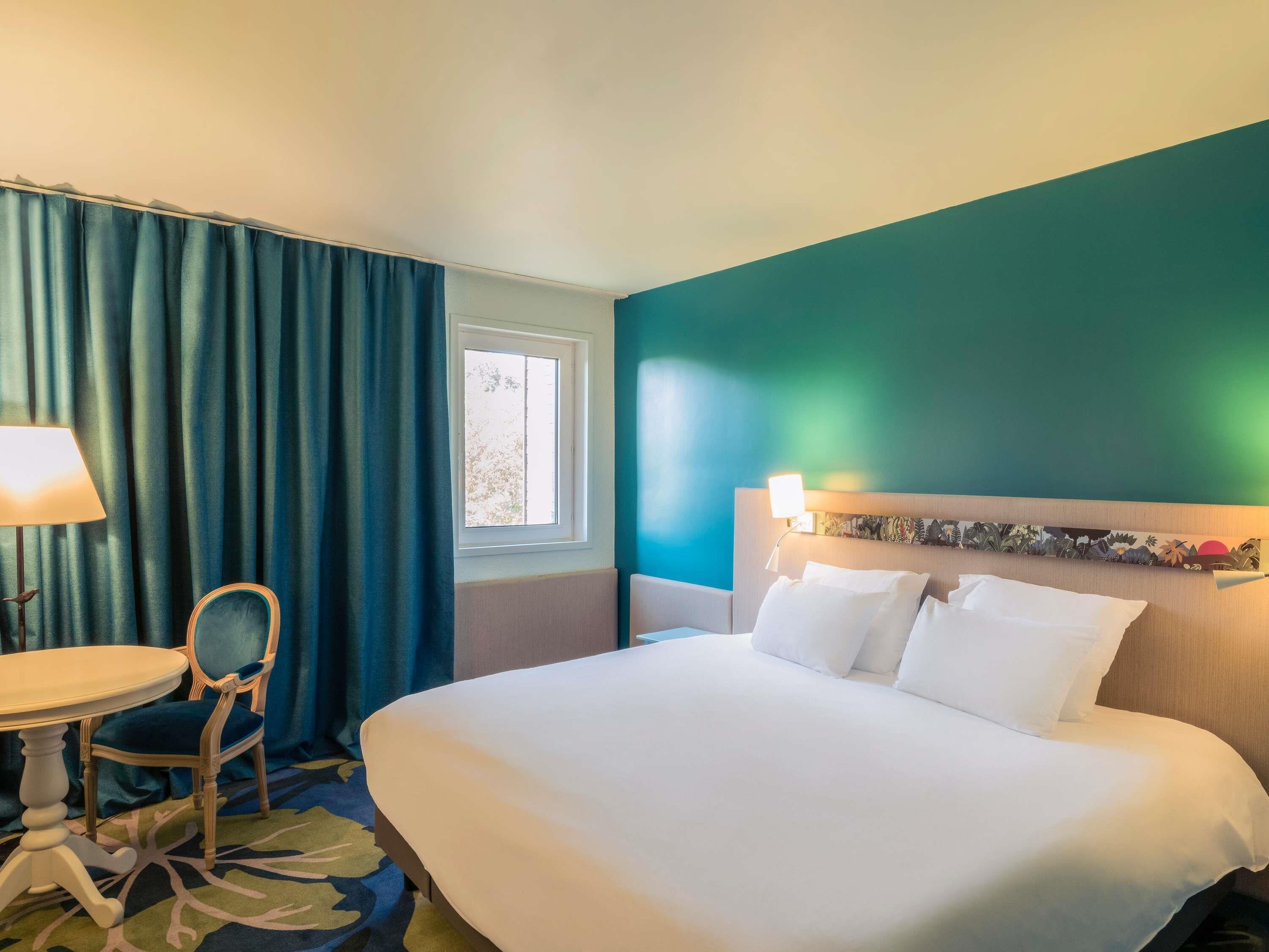 A hotel room with a bed, a desk, a chair, and a window.