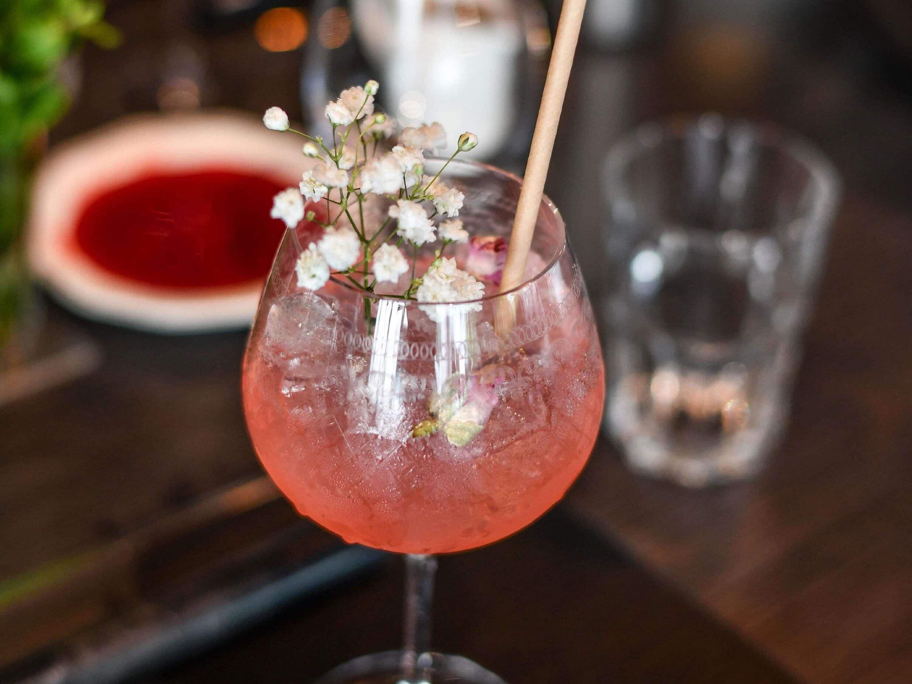 A cocktail glass with ice and a floral garnish on a wooden table.