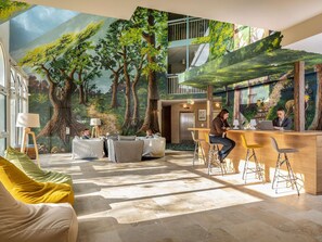 Et hotellobby med et stort mural af en skov, siddepladser og en receptionsdisk.