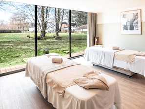 A room with two beds, large windows, a view of a grassy area, and a framed picture on the wall.