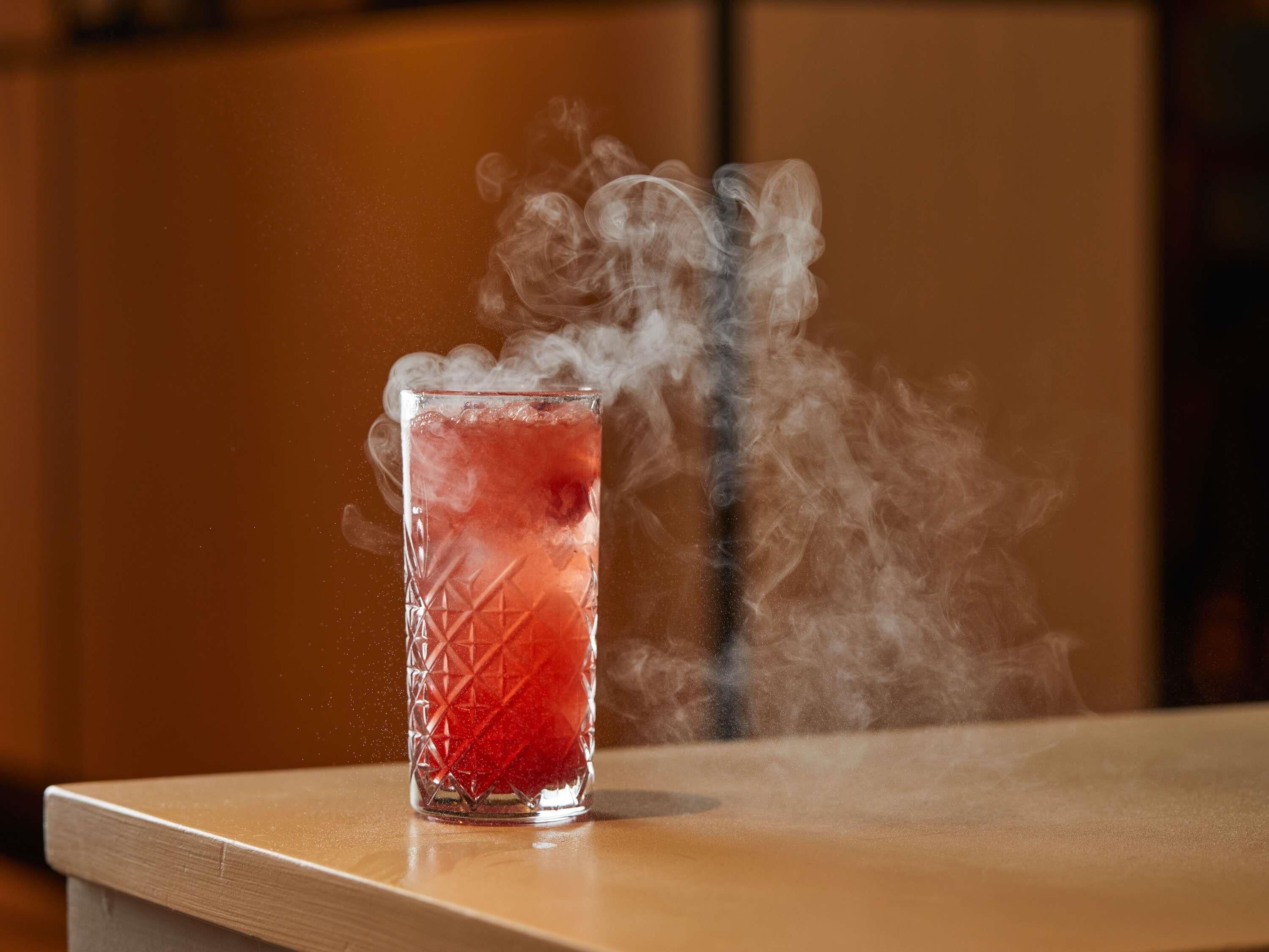 A glass with a red liquid and smoke, placed on a wooden surface.