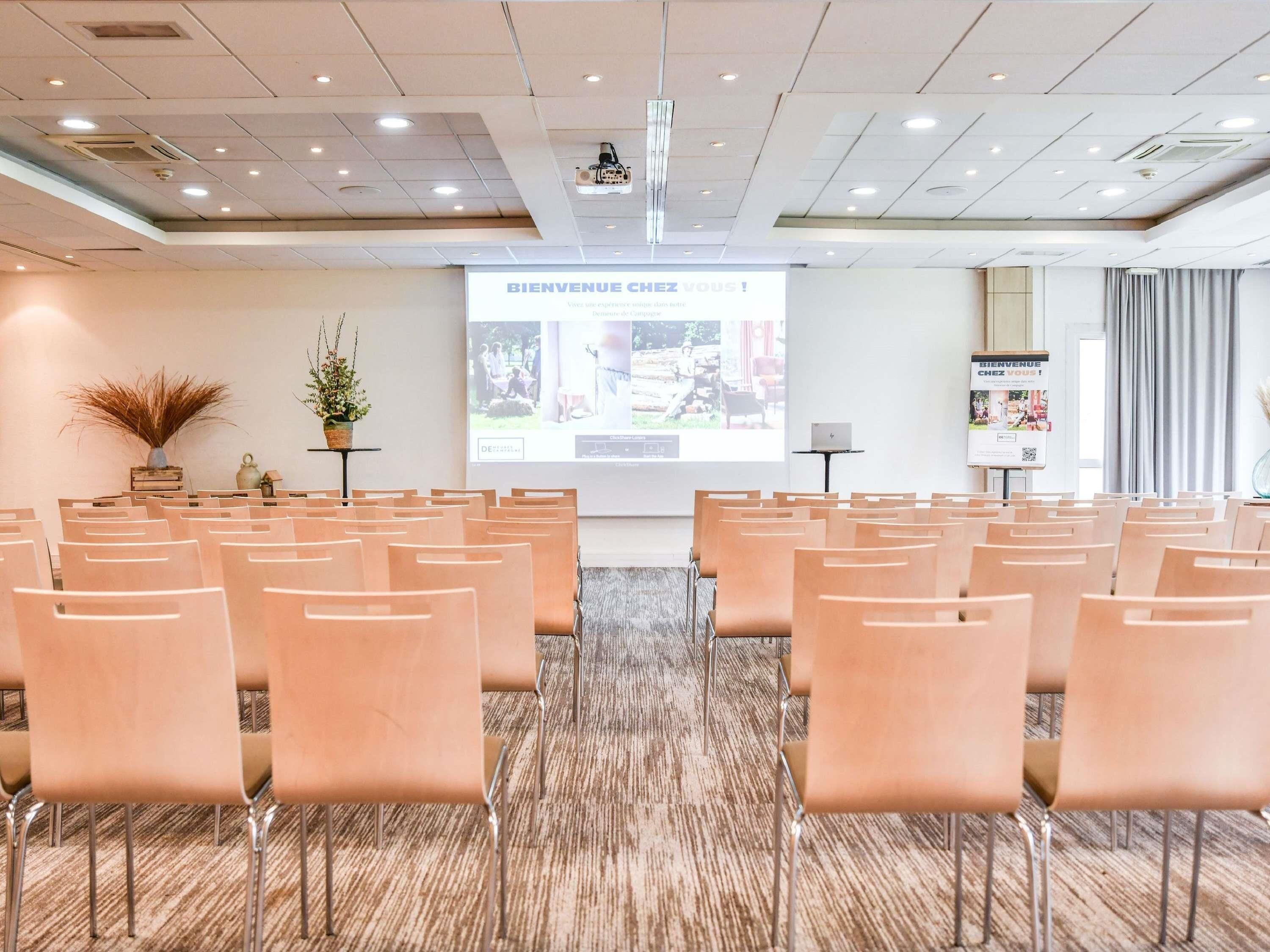 A conference room with rows of chairs, a projector screen, and a welcome sign.