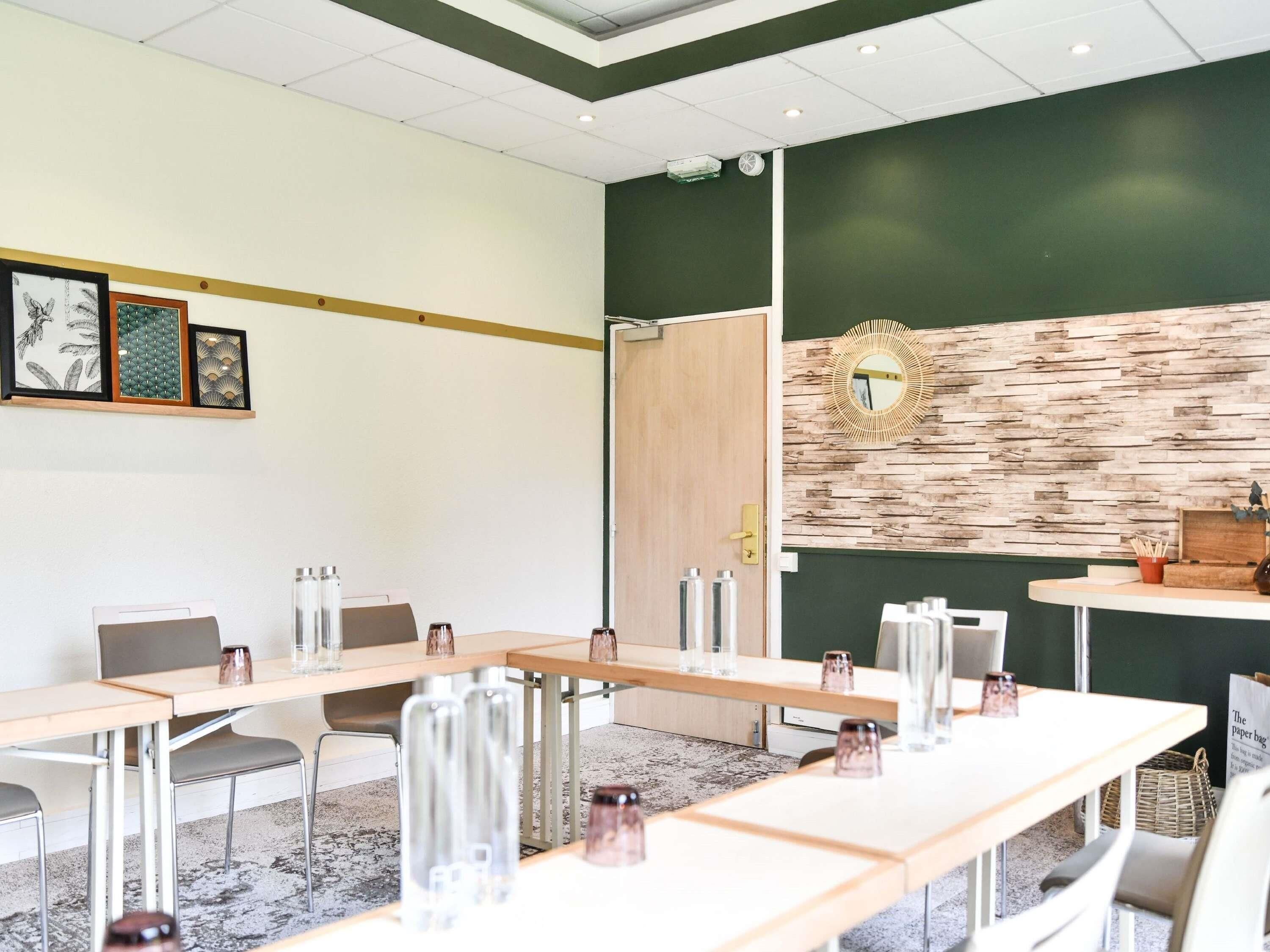 Un salón de conferencias con mesas largas, sillas y un espejo decorativo en la pared.